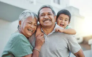 Grandparents, hug and child with smile for happy holiday or weekend break with elderly people at the house. Portrait of grandma and grandpa holding little boy on back for fun playful summer together.